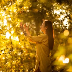 Woman meditating peacefully outdoors in golden sunlight amidst trees.